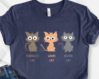 May include: A navy blue t-shirt with a graphic of three cartoon cats representing different mathematical concepts: Fibonacci, Gauss, and Bezier. The text below each cat reads "Fibonacci Cat", "Gauss Cat", and "Bezier Cat".