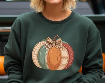 Op de afbeelding: Donkergroene sweatshirt met een decoratief pompoenontwerp. De pompoen bestaat uit verschillende patronen in oranje, groen en beige, met een geruite strik en een steel. Een kledingstuk met herfstthema.