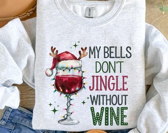 May include: A light gray sweatshirt with the text "MY BELLS DON'T JINGLE WITHOUT WINE." The graphic features a wine glass with a Santa hat and string lights. The sweatshirt is paired with blue jeans and sandals.