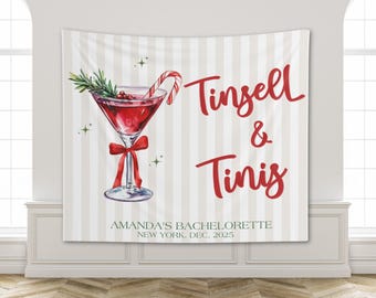 May include: A white and beige striped wall tapestry with a red cocktail illustration. The cocktail has a candy cane, rosemary, and a red bow. Text reads "Tinsell & Tinis" and "Amanda's Bachelorette, New York, Dec, 2025."