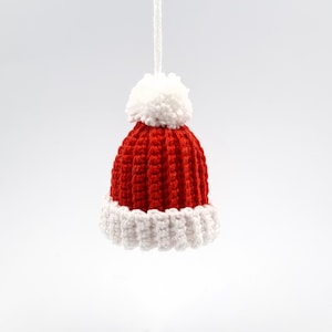 Könnte beinhalten: Eine rote und weiße gehäkelte Weihnachtsmütze mit einem weißen Bommel oben.