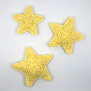 Peut inclure: Trois étoiles jaunes faites à la main au crochet sont disposées sur un fond blanc. Les étoiles ont un design à cinq branches et une surface texturée, probablement réalisée avec un point serré. Les étoiles sont espacées uniformément, créant une esthétique simple et charmante.