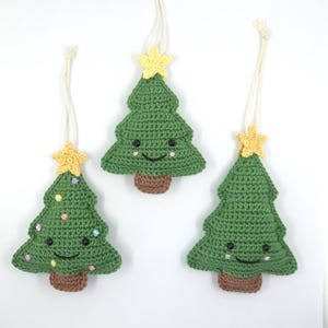 May include: Three handmade green crochet Christmas tree ornaments with smiling faces, brown bases, and yellow star toppers. Each tree has a cream-colored string for hanging. One tree has colorful bead decorations.