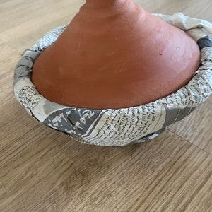May include: A terracotta tagine pot with a lid wrapped in newspaper. The tagine is a traditional Moroccan cooking pot used for slow cooking.