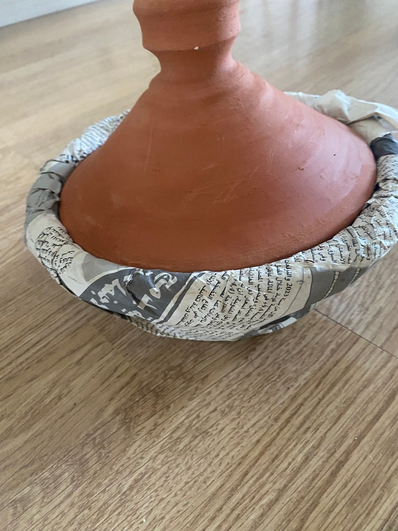 May include: A terracotta tagine pot with a lid wrapped in newspaper. The tagine is a traditional Moroccan cooking pot used for slow cooking.