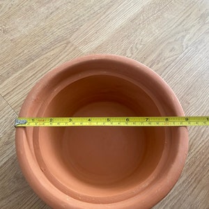 May include: A terracotta flower pot with a diameter of 8 inches. The pot is made of unglazed clay and has a natural brown colour.