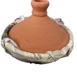 May include: A terracotta tagine cooking pot with a domed lid. The pot is wrapped in newspaper with the text "Home Office Asylur high" visible.