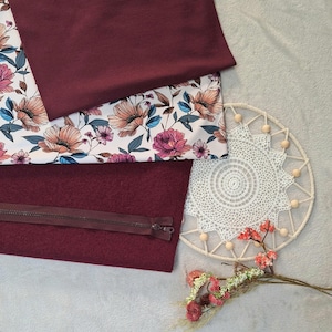 Könnte beinhalten: Eine Auswahl an Stoffstücken in Burgunderrot und floralen Mustern. Ein Stück ist einfarbig burgunderrot, ein anderes hat einen Blumendruck mit rosa, pfirsichfarbenen und blauen Blumen auf weißem Grund. Ein burgunderfarbenes Stück mit Reißverschluss ist ebenfalls vorhanden.