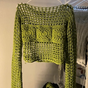 Könnte beinhalten: Ein grünes Häkel-Crop-Top mit langen Ärmeln und einem quadratischen Muster. Das Top hat eine lockere Passform und ist aus einem leichten Material gefertigt.