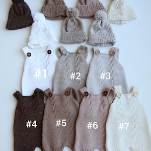 May include: A collection of seven knitted rompers and five matching pom-pom beanies in various neutral shades including white, cream, beige, tan, and dark brown. Each romper features a cable knit pattern, two shoulder buttons, and labels #1-#7.