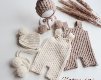 May include: Two ribbed knit rompers with wooden buttons and two matching bonnets with pom-poms in cream and taupe colors. The text "Newborn props From Alida" is visible in the bottom right corner. The items are arranged on a plain white surface.