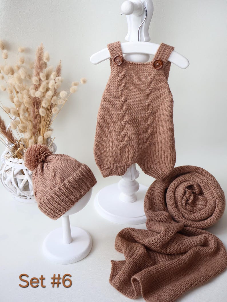 May include: A knitted set in a solid tan color consisting of a sleeveless romper with two brown buttons, a beanie with a pom-pom, and a long scarf. The romper features a vertical cable knit pattern. The text "Set #6" is visible in the bottom left.