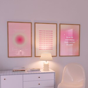 May include: Three framed pink and white motivational posters with inspirational quotes. The left poster has a pink and white gradient background with the text "Dreams Come True". The middle poster has a white background with the text "Believe in your dreams" repeated multiple times. The right poster has a pink and white gradient background with the text "I can do everything that I set my mind to".