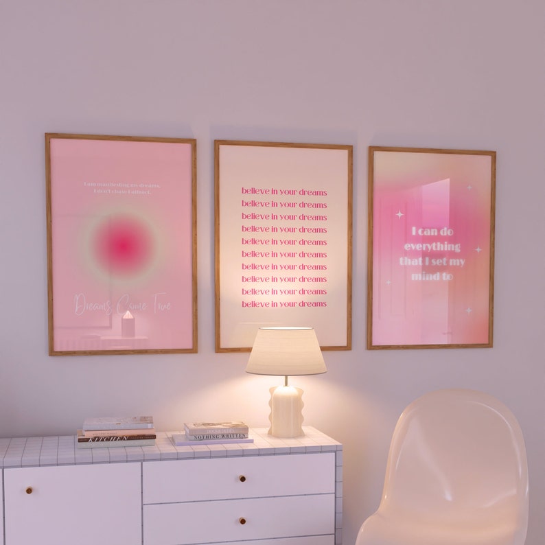May include: Three framed pink and white motivational posters with inspirational quotes. The left poster has a pink and white gradient background with the text "Dreams Come True". The middle poster has a white background with the text "Believe in your dreams" repeated multiple times. The right poster has a pink and white gradient background with the text "I can do everything that I set my mind to".