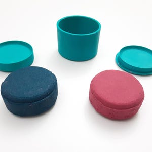 Op de afbeelding: Een bovenaanzicht toont een verzameling turquoise en gekleurde containers en deksels. Er is een turquoise cilinder, twee turquoise deksels en twee ovaalvormige containers, &eacute;&eacute;n blauw en &eacute;&eacute;n rood. De objecten zijn gerangschikt op een wit oppervlak.