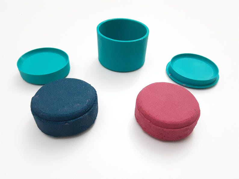 Op de afbeelding: Een bovenaanzicht toont een verzameling turquoise en gekleurde containers en deksels. Er is een turquoise cilinder, twee turquoise deksels en twee ovaalvormige containers, &eacute;&eacute;n blauw en &eacute;&eacute;n rood. De objecten zijn gerangschikt op een wit oppervlak.