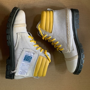 Könnte beinhalten: Ein Paar graue Canvas-Stiefel mit gelben Akzenten und schwarzen Sohlen. Die Stiefel haben ein Etikett mit der Aufschrift "W34 L360" und "SUPER STAR" sowie eine Größentabelle für "WRIST, TRIST, THIGH, LEG,  OPPER STAR, YEAR, TEARS".