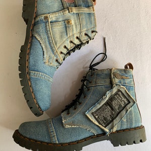 May include: A pair of blue denim boots with black laces and a black rubber sole. The boots have a distressed look with patches of denim sewn on. The right boot has a tag that says "Wrangler Size 38 SKANDERS".