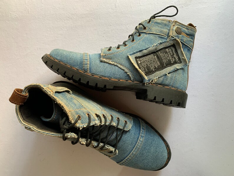 May include: A pair of blue denim boots with black laces and a distressed look. The boots have a black rubber sole and a brown leather accent on the heel.