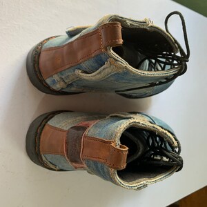 May include: A pair of blue denim ankle boots with brown leather accents. The boots have black laces and a rugged look.