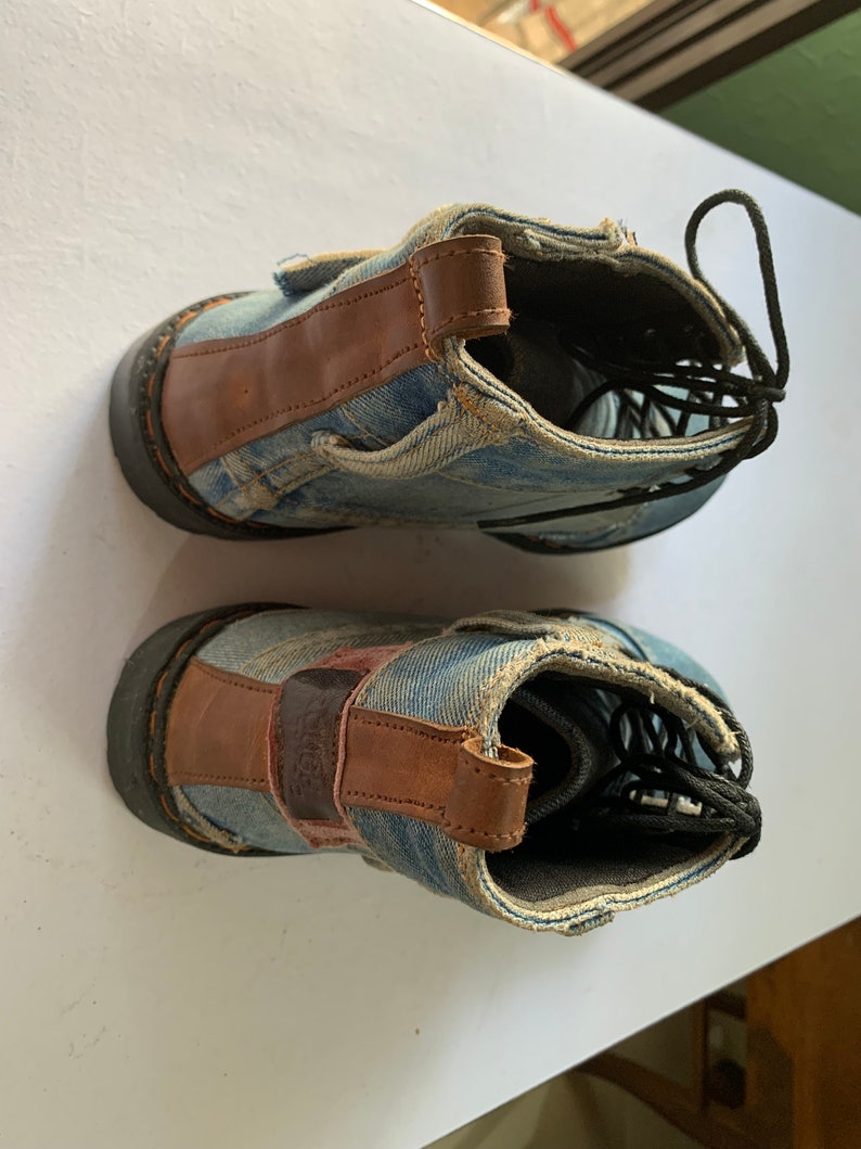 May include: A pair of blue denim ankle boots with brown leather accents. The boots have black laces and a rugged look.