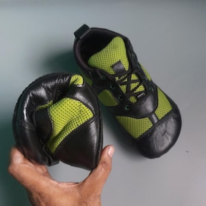 May include: A pair of black and green sneakers with a mesh upper and a lace-up closure. The sneakers are laid out on a gray surface.