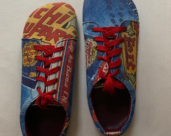 Könnte beinhalten: Ein Paar blaue, rote und gelbe Canvas-Schuhe mit roten Schnürsenkeln. Die Schuhe haben verschiedene bunte Comic-Bilder darauf gedruckt, darunter ein rotes und gelbes Bild einer Banane und die Worte "Go Banana Tie".