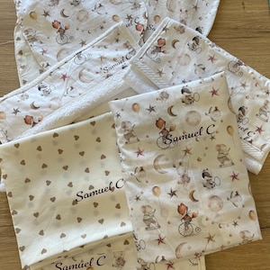 Può includere: Una collezione di biancheria da letto per bambini con un design stravagante. Gli articoli includono bavaglini, coperte e asciugamani, tutti con un motivo ripetuto di animali in bicicletta, lune, stelle e palloncini. Il nome "Samuel C" è stampato.