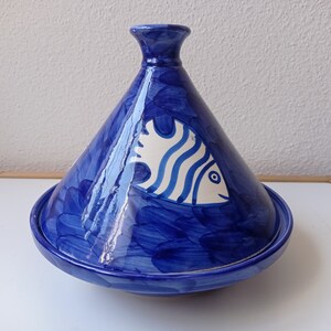 Pode incluir: Tagine de cerâmica azul e branca com um design de peixe. A tagine tem uma tampa cónica e uma base redonda.