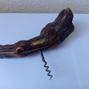 以下が含まれることがあります： 金属製の螺旋状のワインオープナーがついた木製のワインオープナー。木は濃い茶色で、自然で素朴な外観をしています。ワインオープナーには「Vins de la Dourbie - France」というラベルが貼られています。