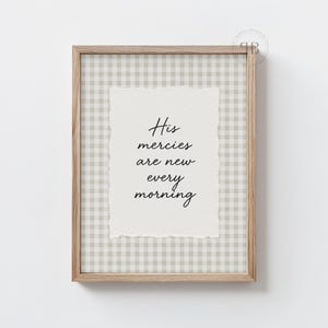 May include: A framed print with the text "His mercies are new every morning" in black script. The print has a torn paper effect and is set against a light green and white checkered background. The frame is made of light-colored wood.