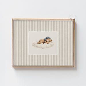 May include: A framed print featuring a watercolor illustration of a sleeping teddy bear on a cloud. The bear wears a blue nightcap. The frame has a gold finish and a striped background.