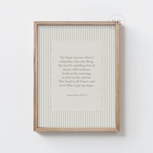 Puede incluir: Una impresión enmarcada con un marco de madera clara. La impresión presenta un fondo texturizado blanquecino con rayas verticales. El centro tiene un papel texturizado blanquecino con texto de Lamentaciones 3:21-24.