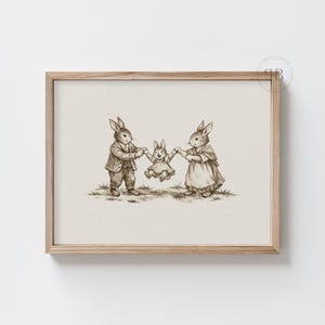 May include: A framed sepia-toned print depicts a family of rabbits. The parents, dressed in vintage clothing, hold the hands of their child, who is suspended mid-air. The artwork is set against a neutral background, framed in light wood.