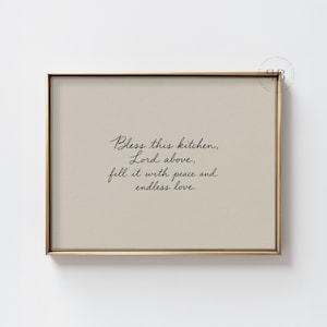 Könnte beinhalten: Ein gerahmter Druck mit einem goldfarbenen Rahmen. Der Druck hat einen beigefarbenen Hintergrund mit schwarzem Kursivtext, der lautet: "Bless this kitchen, Lord above, fill it with peace and endless love."