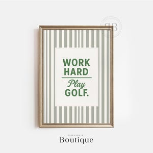 Könnte beinhalten: Ein goldfarbener gerahmter Druck mit einem weißen und grauen gestreiften Hintergrund. Der Druck hat einen weißen Kasten mit dem Text "Work Hard Play Golf." in grünen Buchstaben.