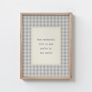 May include: A framed print with a light wood frame. The print features a light blue and white gingham pattern surrounding a cream-colored rectangle with the text: "How wonderful life is now you're in the world."