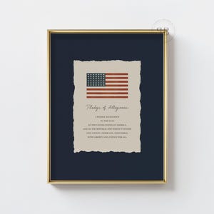 Può includere: Stampa incorniciata con cornice dorata, raffigurante la bandiera americana e il Giuramento di Fedeltà. La bandiera è rossa, bianca e blu, su sfondo blu scuro. Il testo è in un classico carattere serif.
