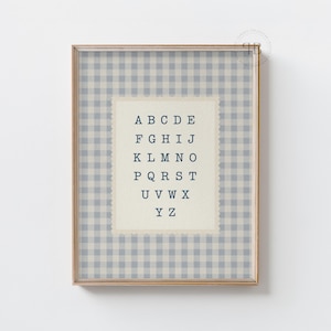 May include: A framed print featuring the alphabet in a vintage style. The background has a blue and white gingham pattern. The alphabet is printed in a dark blue font on a cream-colored background.