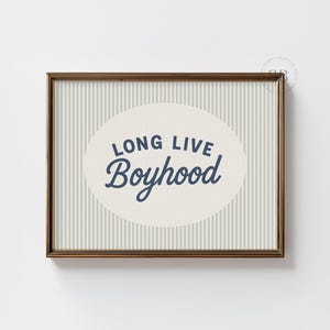 May include: Framed art print with a gold-colored frame. The artwork features the text "LONG LIVE Boyhood" in a navy blue script within an oval shape, set against a striped background.