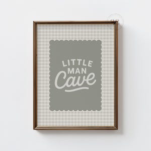 Könnte beinhalten: Gerahmtes Wandbild mit dem Text "LITTLE MAN CAVE" in einer verspielten Schriftart. Das Kunstwerk ist vor einem grauen Hintergrund mit einem gewellten Rand, in einem braunen Rahmen und einem karierten Muster angeordnet.
