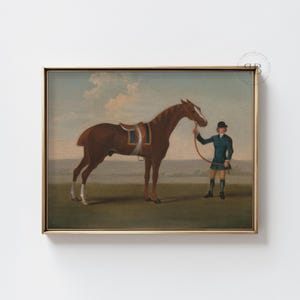 May include: A framed vintage painting of a brown horse with a saddle, held by a person in a blue coat and black hat. The artwork is set against a field and sky, framed in a gold tone. The painting is a classic equestrian scene.