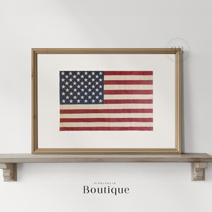 May include: A framed print of an old, faded American flag with red, white, and blue stripes and white stars on a blue field. The flag is displayed on a wooden shelf.