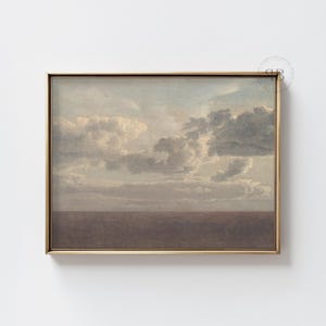 May include: A framed art print depicting a cloudy sky over a brown horizon. The artwork is in a gold-coloured frame. The print has a vintage aesthetic, with soft colours and a serene atmosphere.