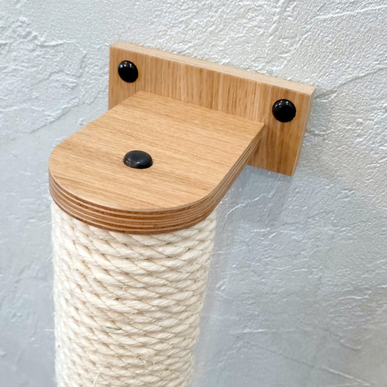 May include: A wooden cat scratching post with a natural wood finish and a thick rope covering. The post is mounted to a wall with a bracket and screws.