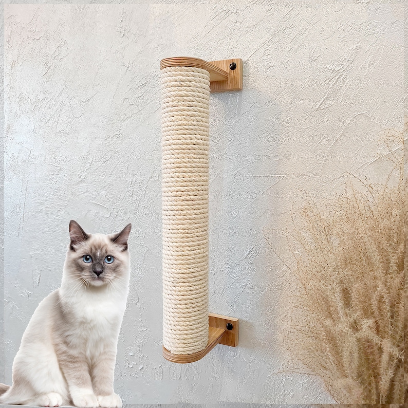 May include: A beige cat scratching post with a natural rope covering. The post is mounted to a wall with a wooden bracket. A white cat with blue eyes sits in front of the post.