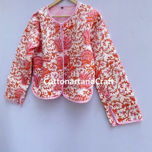 May include: Quilted jacket with a floral pattern in shades of orange and pink on a white background. The jacket has a round neckline, long sleeves, and a pink trim. The text "CottonartandCraft" is visible.