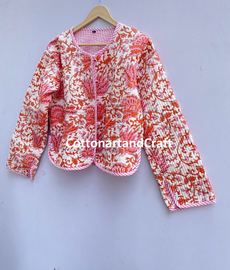 May include: Quilted jacket with a floral pattern in shades of orange and pink on a white background. The jacket has a round neckline, long sleeves, and a pink trim. The text "CottonartandCraft" is visible.