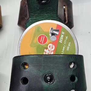 May include: A dark green leather pouch with a brown leather belt loop. The pouch holds a tin of 4.5mm pellets. The tin is orange and green with the text "ECON II".