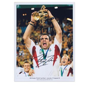 May include: A black and white photograph of a rugby player holding aloft the Rugby World Cup trophy. The player is wearing a white jersey with the England team logo. The photo is signed by the player, Martin Johnson, and includes the text "2003 Rugby World Cup Final - Australia 17 England 29".